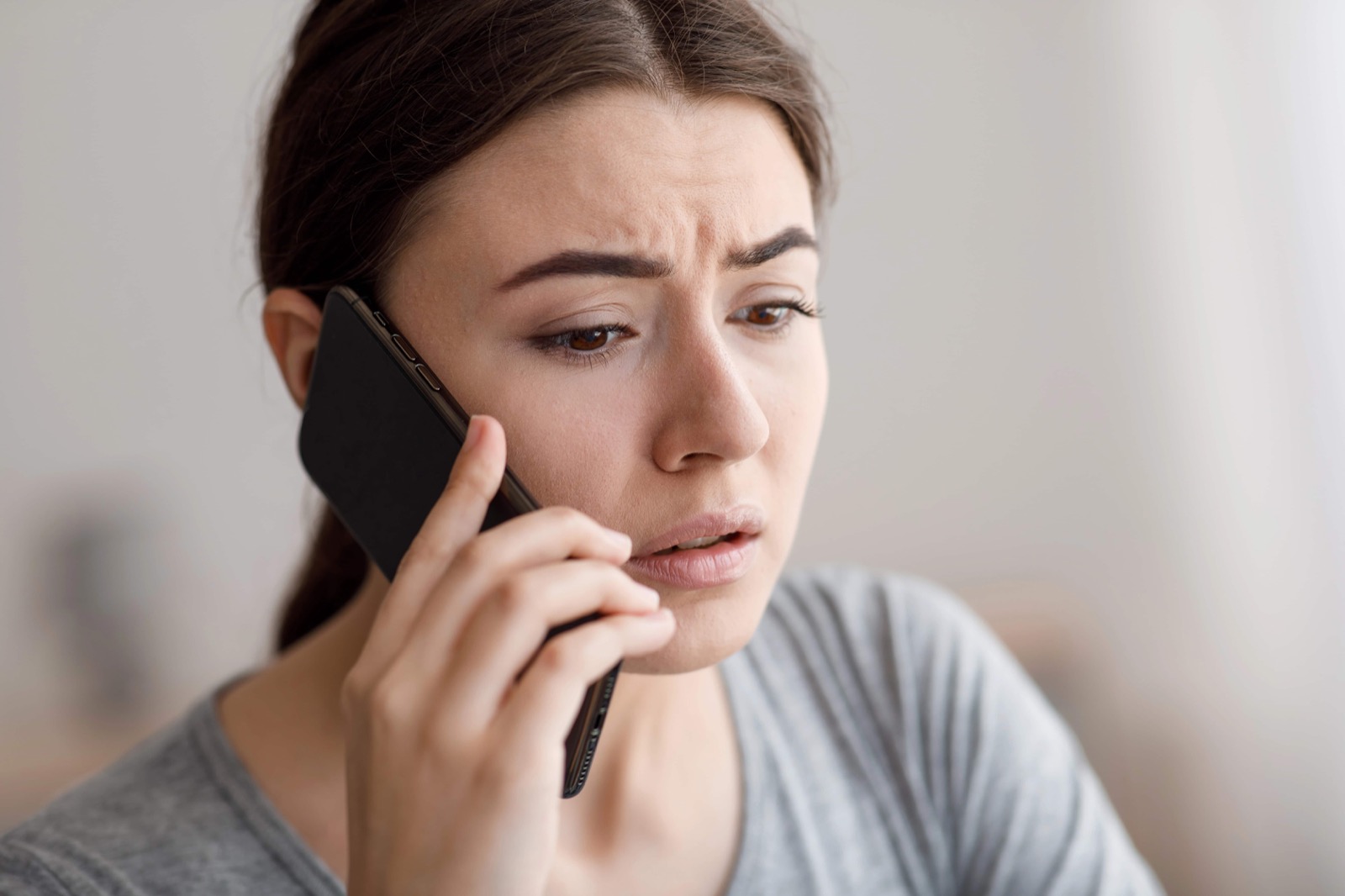 Eine angespannte Frau hält ein Smartphone ans Ohr und blickt nachdenklich zur Seite.