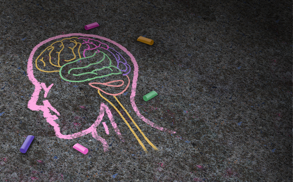 Eine farbige Kreidezeichnung eines Gehirns auf einem Asphaltweg, umgeben von verschiedenen Kreidestücken.