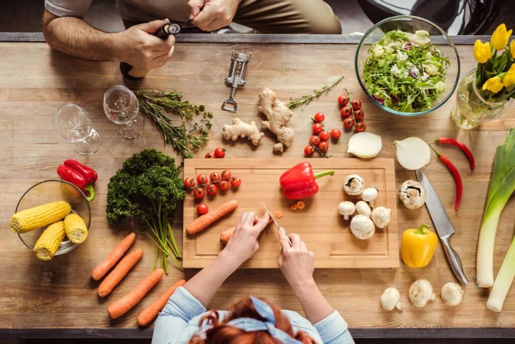 Oberansicht einer Arbeitsfläche, auf der verschiedene frische Zutaten wie Gemüse, Kräuter und Salat für die Zubereitung eines gesunden Gerichts vorbereitet werden – ein Symbol für die Bedeutung einer ausgewogenen Ernährung bei hochsensiblen Menschen (HSP) zur Stabilisierung von Energie und Wohlbefinden.