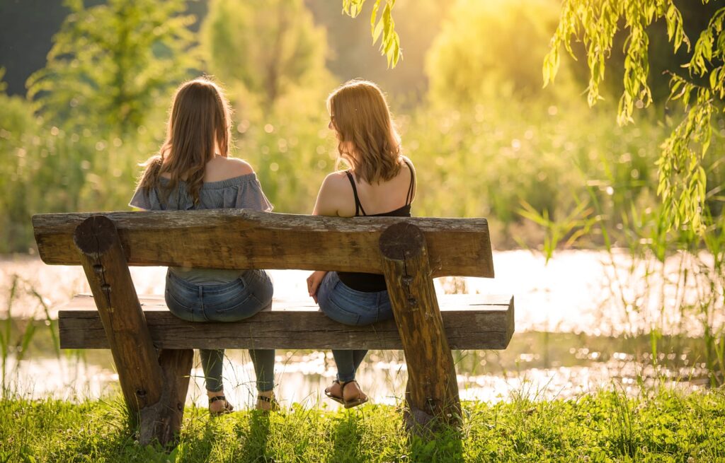 Zwei Frauen sitzen auf einer Holzbank am See und führen ein ruhiges Gespräch bei Sonnenuntergang.