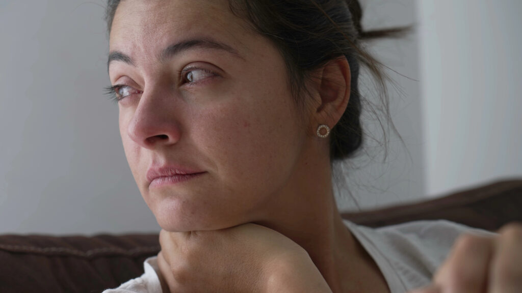 Frau mit nachdenklichem, angespanntem Blick, Kinn auf der Schulter abgestützt, Blick zur Seite gerichtet – Symbolbild emotionale Überforderung