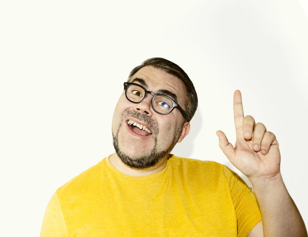 Lachender Mann mit erhobenem Finger in gelbem Shirt – Symbol für spontane Ideen und übersprudelnde Vielseitigkeit
