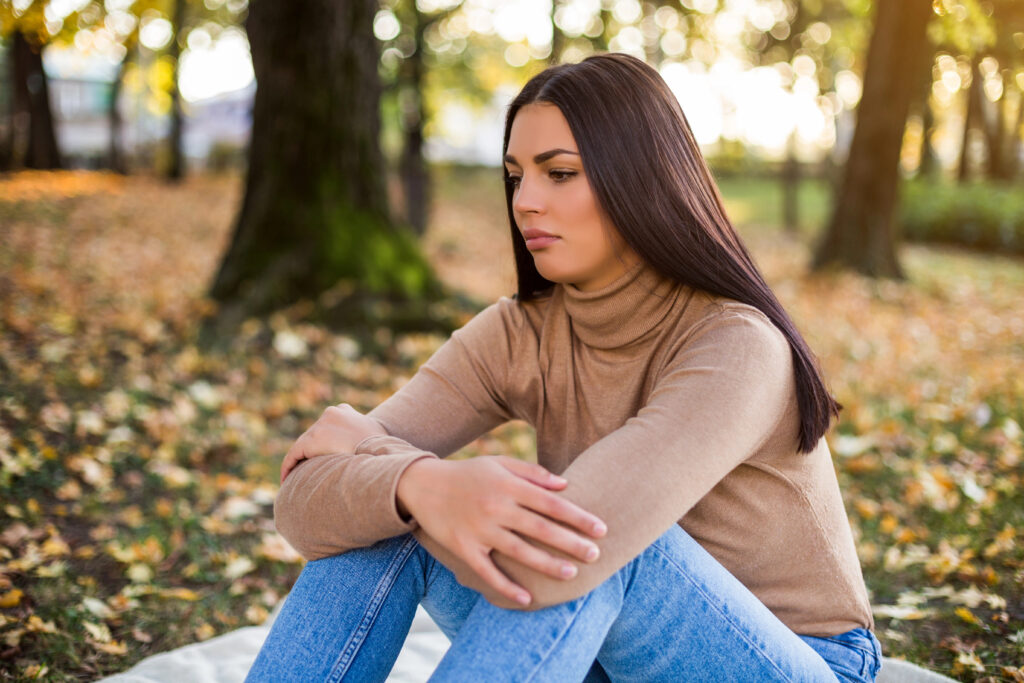 Nachdenkliche Frau sitzt im Park und schaut nachdenklich zur Seite – Symbolbild für Entscheidungsschwierigkeiten bei hochsensiblen Scannerinnen.