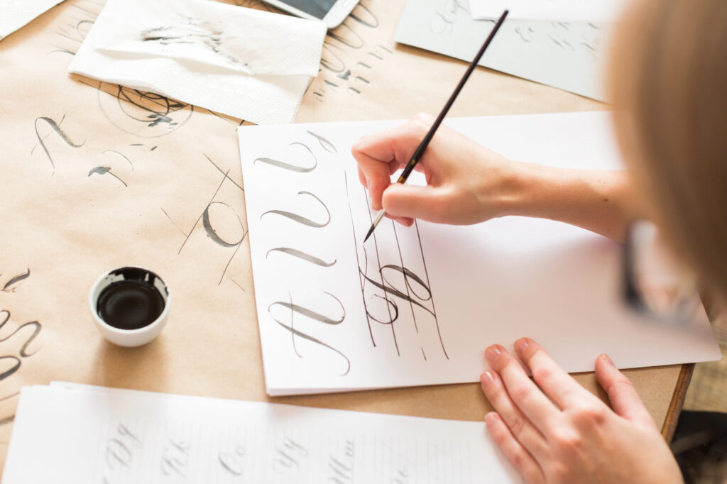 Nahaufnahme einer Person, die sorgfältig Kalligrafie-Zeichen auf ein Blatt Papier malt – symbolisiert die Praxis des langsamen Forschens.