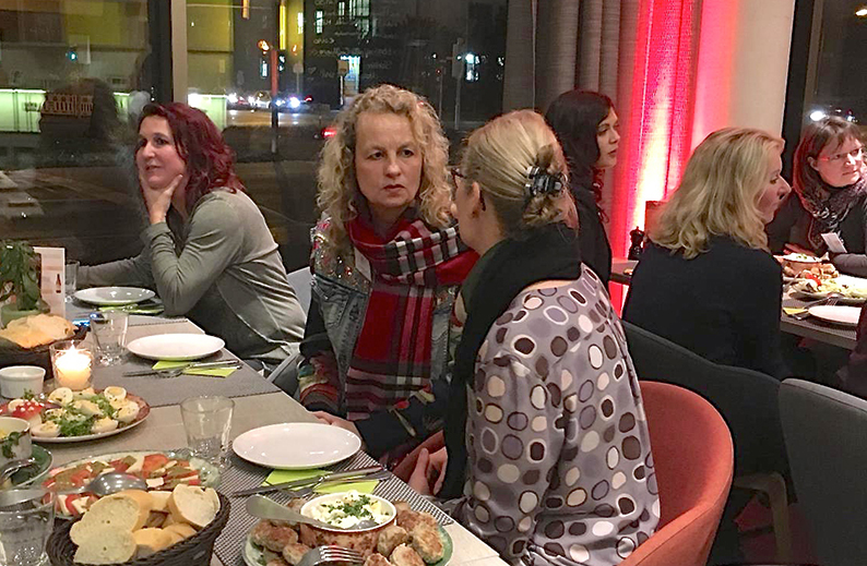Mehrere Frauen sitzen beim Abendessen an einem Tisch und führen intensive Gespräche in entspannter Atmosphäre.