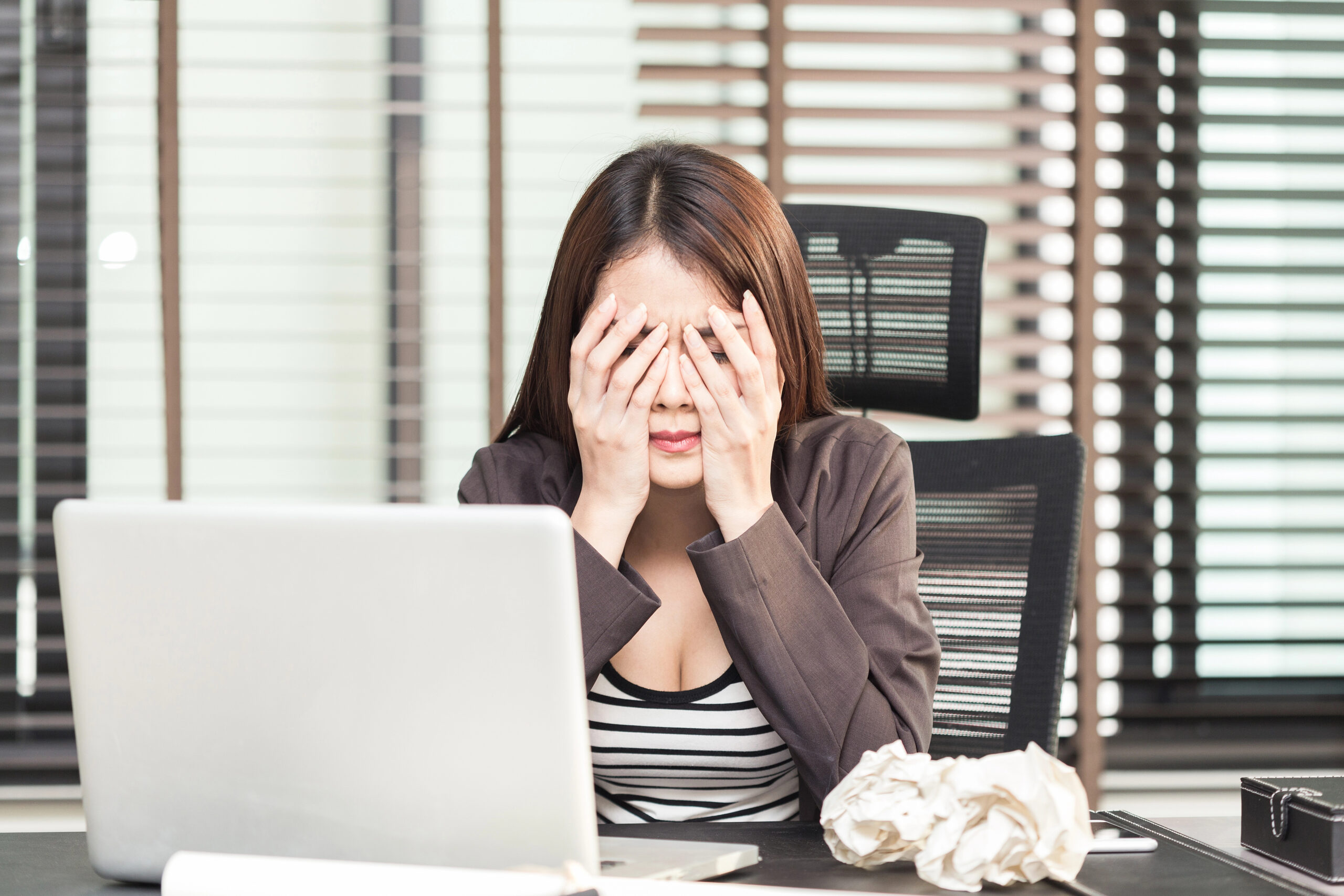 Erschöpfte Frau sitzt am Schreibtisch mit den Händen vor dem Gesicht – Symbolbild für Selbstüberforderung bei vielbegabten Scanner-Persönlichkeiten.
