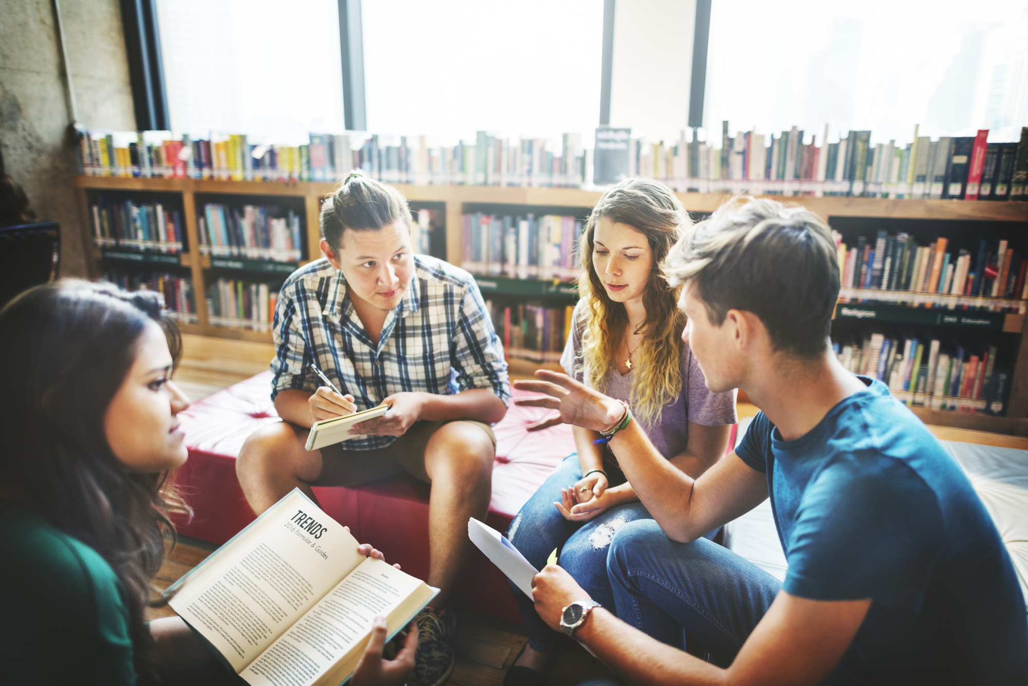 Eine Gruppe junger Erwachsener sitzt zusammen in einer Bibliothek und diskutiert engagiert über ein Thema.