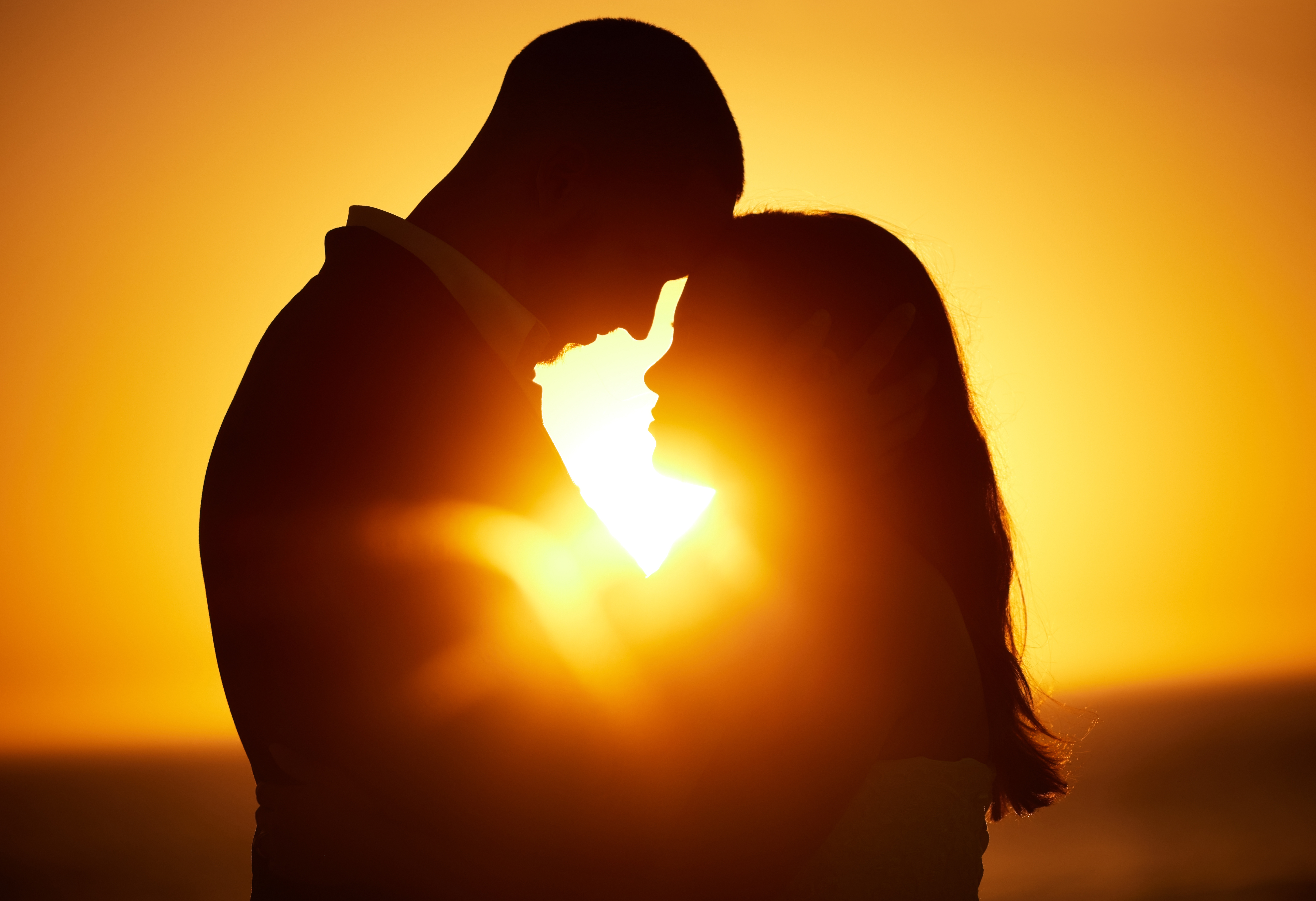 Zwei Personen sind - ineinander versunken - voe einem Sonnenuntergang als Silohette zu sehen
